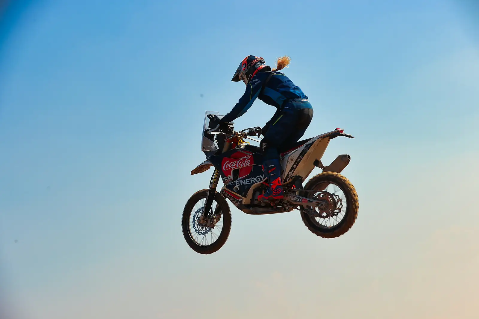 Jasmin Riccius mid-air on the rally bike against an open sky